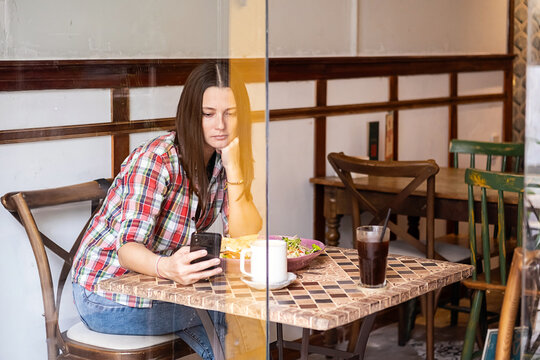 Brunette woman uses smartphone while sitting in cafe in the morning.