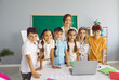 © Studio Romantic - Happy group children of elementary school students and friendly casual female teacher posing during computer literacy lesson standing in classroom with blackboard. Education, back to school
