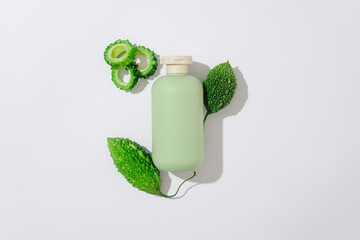 Sticker - Top view of a green bottle without label container shampoo or shower gel decorated with fresh bitter melon and bitter melon slices on white background. Mockup scene for advertising, space for design