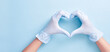 Doctor's hands in medical gloves in shape of heart on blue background with copy space. Health concept