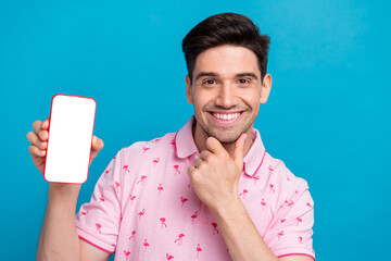 Poster - Portrait of nice creative minded man arm touch chin showing empty space smart phone screen isolated on blue color background