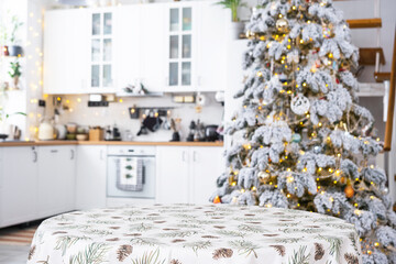 Wall Mural - Round empty table to demonstrate the product with with tablecloth with pine needles and cones print, space for text in white kitchen, modern interior with a Christmas tree. New Year, Christmas