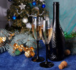 Two glasses of champagne, a bottle, a decorated Christmas tree on blue.