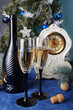 Two glasses of champagne, a bottle, an antique mantel clock, a decorated Christmas tree on blue.