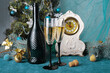 Two glasses of champagne, a bottle, an antique mantel clock, a decorated Christmas tree on blue.