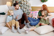 © RVSTOCK - family time on christmas holiday, sit together on floor near decorated christmas tree. dad tell the story and fairy tales to the kids. children listen and mom is smiling.