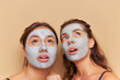© South House Studio - Two girls wearing makeup masks posing on background, looking up in surprise, healthcare products concept, copy space
