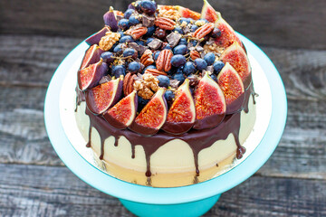 Wall Mural - Delicious cake with figs dipped into melted chocolate, pecan nuts, grapes, chocolate bites and cookies on the top. Concept of autumn or summer cake