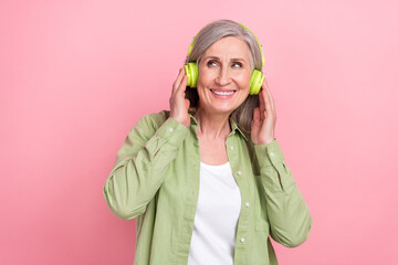 Wall Mural - Photo of cheerful dreamy lady wear green stylish clothes hands touch mp3 player look up offer empty space isolated on pink color background