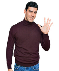 Wall Mural - Handsome hispanic man wearing casual turtleneck sweater showing and pointing up with fingers number five while smiling confident and happy.