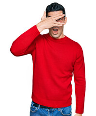 Wall Mural - Handsome hispanic man wearing casual clothes and glasses peeking in shock covering face and eyes with hand, looking through fingers with embarrassed expression.