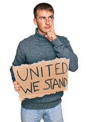 Poster - Young blond man holding united we stand banner serious face thinking about question with hand on chin, thoughtful about confusing idea