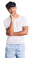 Wall Mural - Young hispanic man wearing casual clothes looking confident at the camera with smile with crossed arms and hand raised on chin. thinking positive.