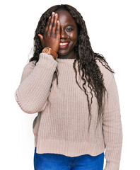 Poster - Young african woman wearing wool winter sweater covering one eye with hand, confident smile on face and surprise emotion.