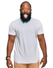 Poster - Young african american man wearing casual white tshirt sticking tongue out happy with funny expression. emotion concept.