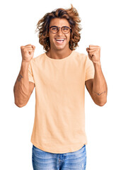 Wall Mural - Young hispanic man wearing casual clothes and glasses celebrating surprised and amazed for success with arms raised and open eyes. winner concept.