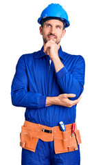 Canvas Print - Young handsome man wearing worker uniform and hardhat with hand on chin thinking about question, pensive expression. smiling and thoughtful face. doubt concept.