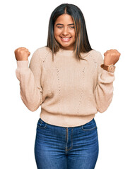 Wall Mural - Young latin girl wearing wool winter sweater excited for success with arms raised and eyes closed celebrating victory smiling. winner concept.