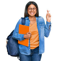 Poster - Young latin girl wearing student backpack and holding books gesturing finger crossed smiling with hope and eyes closed. luck and superstitious concept.