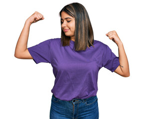 Canvas Print - Young hispanic girl wearing casual purple t shirt showing arms muscles smiling proud. fitness concept.