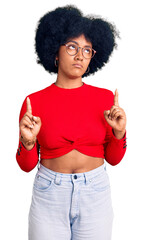 Canvas Print - Young african american girl wearing casual clothes and glasses pointing up looking sad and upset, indicating direction with fingers, unhappy and depressed.