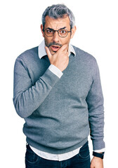 Wall Mural - Middle age hispanic with grey hair wearing glasses looking fascinated with disbelief, surprise and amazed expression with hands on chin