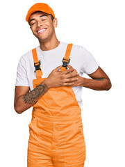 Wall Mural - Young handsome african american man wearing handyman uniform smiling with hands on chest with closed eyes and grateful gesture on face. health concept.