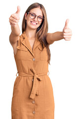 Wall Mural - Young beautiful blonde woman wearing casual clothes and glasses approving doing positive gesture with hand, thumbs up smiling and happy for success. winner gesture.