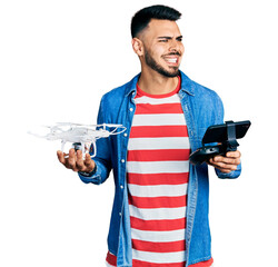 Wall Mural - Young hispanic man with beard using drone with remote control angry and mad screaming frustrated and furious, shouting with anger. rage and aggressive concept.