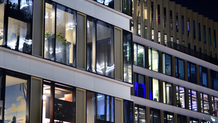 Wall Mural - Fragment of the glass facade of a modern corporate building at night. Modern glass office  in city. Big glowing windows in modern office buildings at night, in rows of windows light shines. 