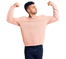 Poster - Young hispanic man wearing casual clothes showing arms muscles smiling proud. fitness concept.