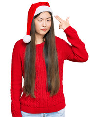 Poster - Young chinese woman wearing christmas hat shooting and killing oneself pointing hand and fingers to head like gun, suicide gesture.