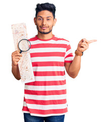 Wall Mural - Handsome latin american young man looking at city map with magnifying glass smiling happy pointing with hand and finger to the side