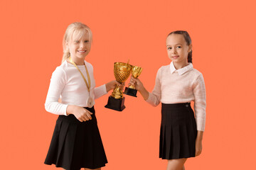 Wall Mural - Smart little classmates in stylish uniform with prize cups and medal on orange background