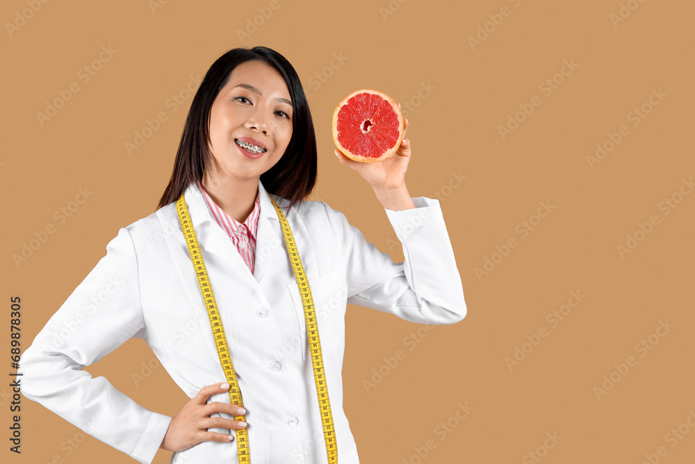 Female Asian nutritionist with grapefruit on beige background