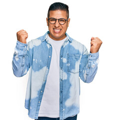 Wall Mural - Young latin man wearing casual clothes and glasses screaming proud, celebrating victory and success very excited with raised arms