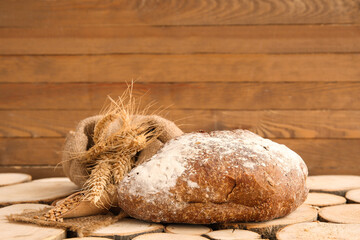 Loaves of fresh bread with wheat spikelets and grains on wooden background