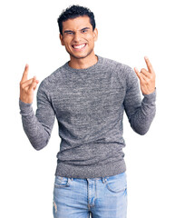 Sticker - Hispanic handsome young man wearing casual sweater shouting with crazy expression doing rock symbol with hands up. music star. heavy concept.