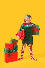 Sticker - Beautiful young woman dressed as elf with Christmas gifts on yellow background