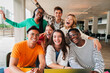 © Jose Calsina - Group of young teenage students siting at library, using a laptop and looking at camera. Happy classmates studying and doing homeworks at high school. Multiracial academy people portrait. Schoolboys