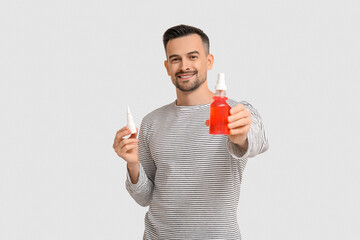 Poster - Sick young man with nasal drops and spray for sore throat on light background