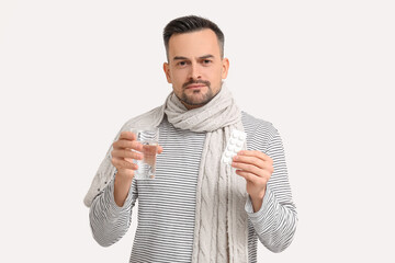 Poster - Sick young man in scarf with pills and glass of water on light background