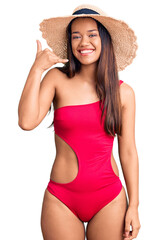 Wall Mural - Young beautiful latin girl wearing swimwear and summer hat smiling doing phone gesture with hand and fingers like talking on the telephone. communicating concepts.