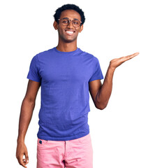 Wall Mural - African handsome man wearing casual clothes and glasses smiling cheerful presenting and pointing with palm of hand looking at the camera.