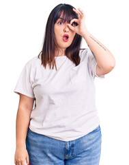 Canvas Print - Young plus size woman wearing casual clothes doing ok gesture shocked with surprised face, eye looking through fingers. unbelieving expression.