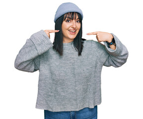 Poster - Young hispanic woman wearing cute wool cap smiling cheerful showing and pointing with fingers teeth and mouth. dental health concept.