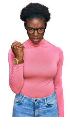 Wall Mural - Young african american girl wearing casual clothes and glasses angry and mad raising fist frustrated and furious while shouting with anger. rage and aggressive concept.