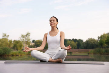 Canvas Print - Beautiful young woman practicing Padmasana on yoga mat outdoors, low angle view. Lotus pose