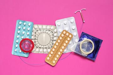 Wall Mural - Contraceptive pills, condoms and intrauterine device on pink background, flat lay. Different birth control methods