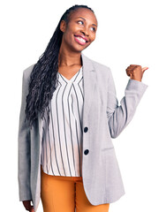 Sticker - Young african american woman wearing business clothes smiling with happy face looking and pointing to the side with thumb up.